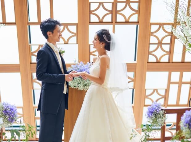 陽射しが差し込むチャペルに立ち互いを見つめ合い手を繋ぐタキシードの新郎とウェでドレスの新婦
